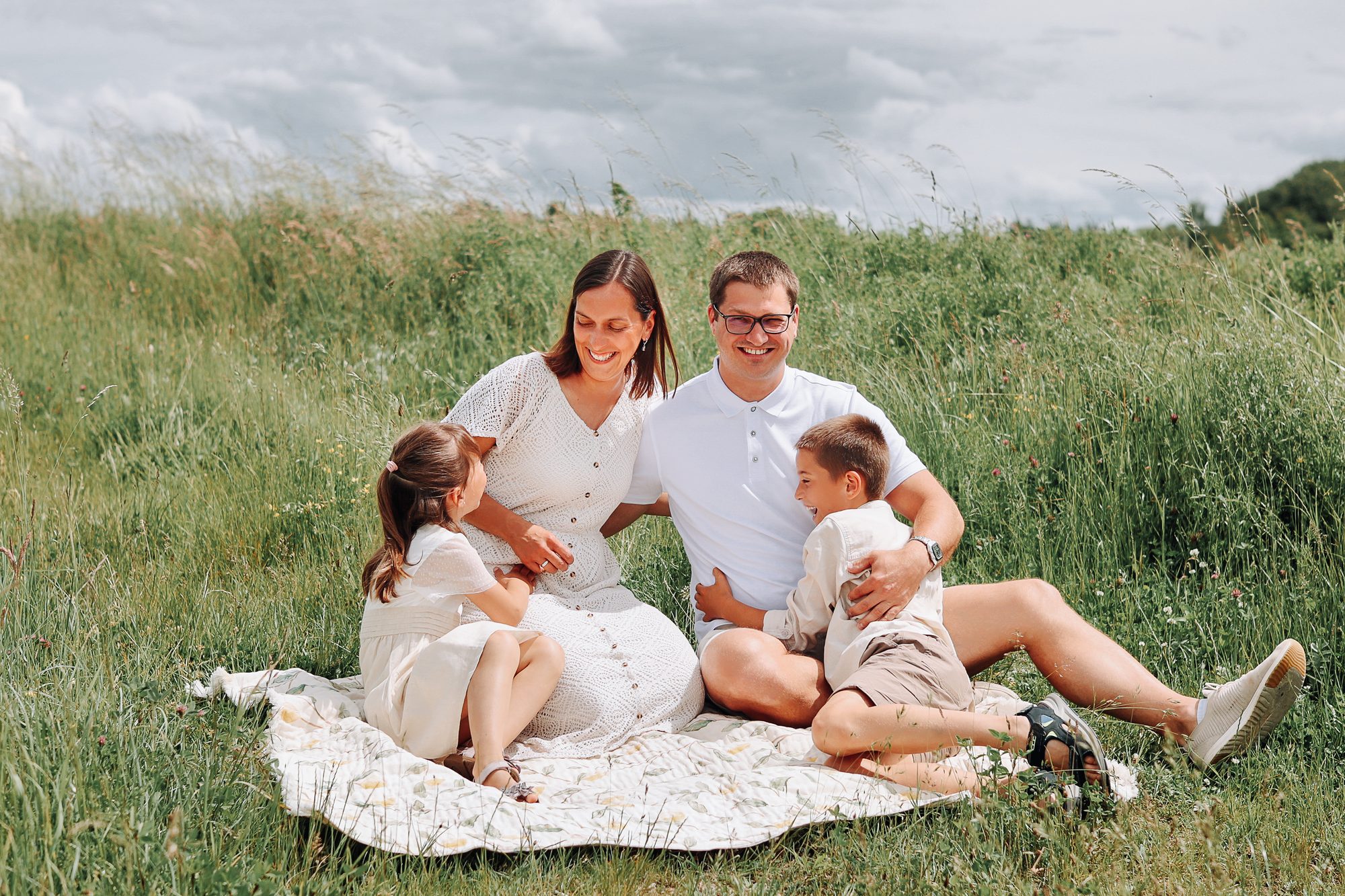 Familienshooting outdoor in Duingen: Eltern und Kinder lachen zusammen auf der Picknickdecke